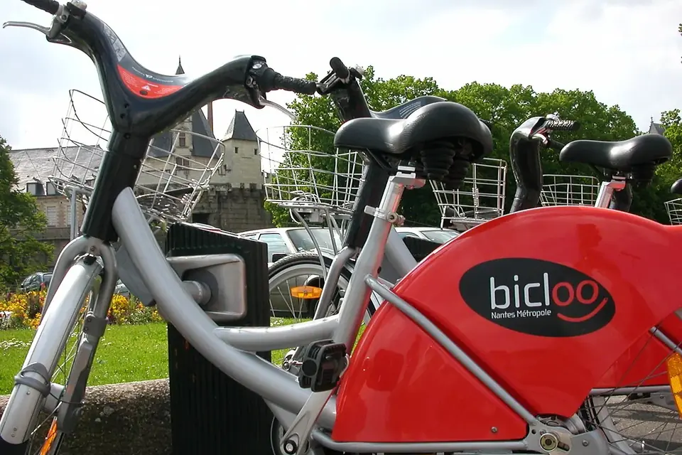 Vélos en libre-service rouges garés à leur station, avec le château des ducs de Bretagne en arrière-plan