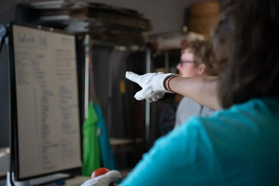 Une personne en gants blancs désigne un tableau où est inscrite la liste des produits de la semaine, lors d'une distribution de paniers