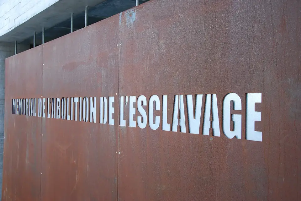 Un grand panneau d'acier rouillé portant en lettres blanches l'inscription Mémorial de l'abolition de l'esclavage
