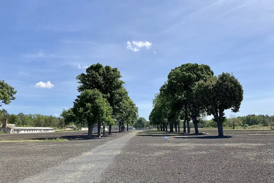 Une large allée de gravier bordée d'arbres sous un ciel bleu, sur le site de l'ancien camp de Ravensbrück