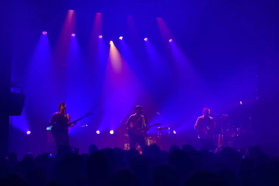 Un groupe de rock sur scène dans une salle plongée dans une lumière bleue et violette, le public au premier plan